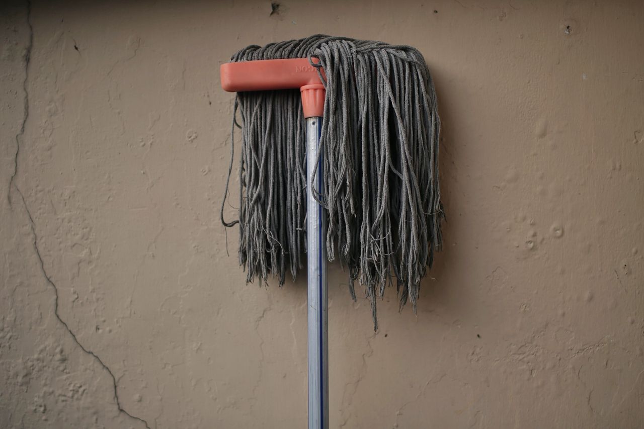 A gray mop rests against a textured wall, suggesting a simple domestic scene.